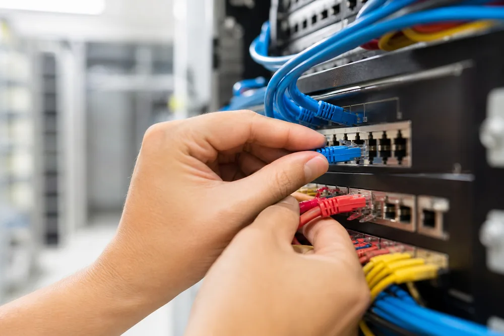 Hände stecken Patchkabel in ein Netzwerk-Patchpanel